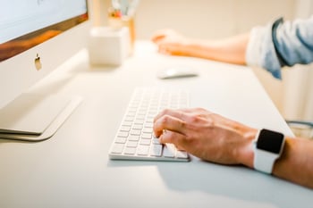 Handing typing on a keyboard with iMac showing on white desk