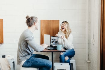 Two people laughing together by a computer at work